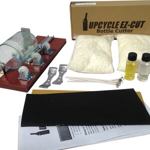 May include: Upcycle EZ-Cut bottle cutter kit. Includes a wooden base with rollers, glass bottle, wax, wicks, and other supplies. The box has the text "Upcycle EZ-Cut Bottle Cutter".