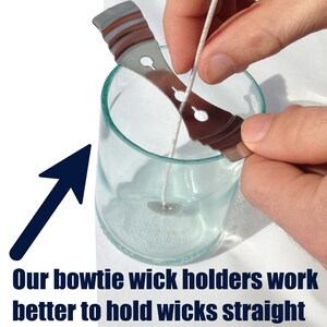 May include: A silver metal bowtie wick holder is being used to hold a white wick straight in a clear glass jar. The wick holder is designed to keep the wick centered in the jar and prevent it from moving around.