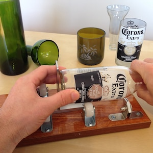 Puede incluir: Una persona utiliza un cortador de botellas para crear un vaso a partir de una botella de cerveza Corona Extra. La configuraci&oacute;n incluye una base de madera, componentes met&aacute;licos y un vaso transparente. Se ven otros objetos de vidrio cortado.