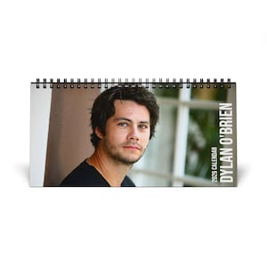 May include: A 2026 calendar featuring a portrait of Dylan O'Brien. The calendar is spiral-bound and has a white background. The text "2026 CALENDAR" and "DYLAN O'BRIEN" are printed on the right side of the calendar.