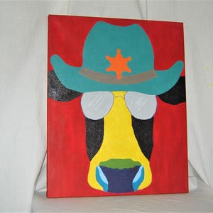 May include: A colorful painting of a cow wearing a turquoise cowboy hat with a sheriff's star and sunglasses. The cow's face is yellow with black markings and a green and blue nose. The background is red.