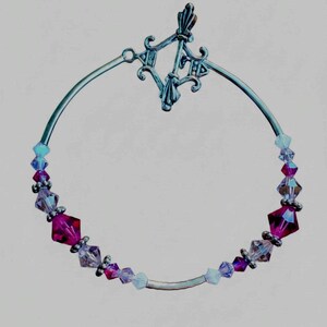 May include: A circular bracelet featuring a silver-toned metal toggle clasp with ornate detailing. The band is composed of alternating faceted crystal beads in shades of deep magenta, light lavender, and pale blue, separated by small silver spacers.