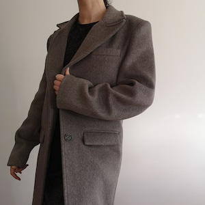 May include: A long, grey wool coat with a single button fastening and a patch pocket on the left side.