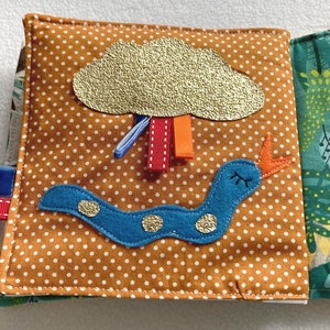 May include: A brown fabric book with a blue and orange worm, a gold glitter cloud with red and orange ribbons, and a green fabric background with a leaf pattern.