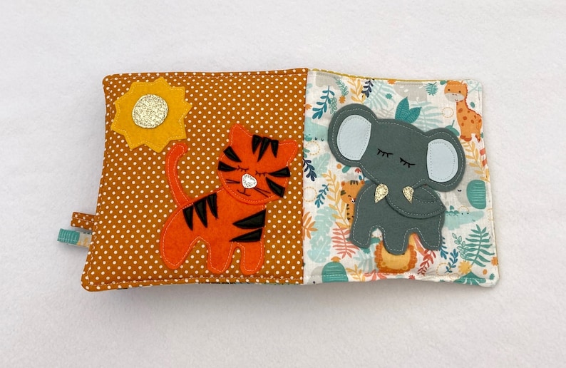 May include: A brown and orange fabric book with a tiger and a sun on one side and an elephant and jungle leaves on the other side.