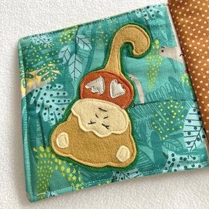 May include: A soft, green fabric book with a brown felt monkey appliqu&eacute;. The monkey has a long tail, a brown felt head, and a silver felt heart on its chest. The book is perfect for babies and toddlers.