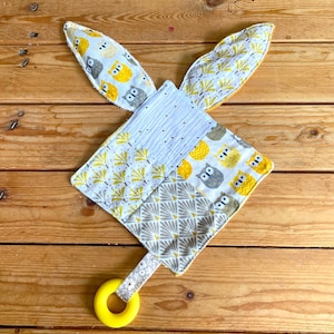 May include: A yellow and gray baby toy with a textured fabric and owl print. The toy has a yellow teething ring attached to it.