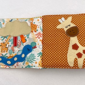 May include: A soft, multi-page book for babies and toddlers features a colorful jungle scene with a blue snake, a cloud, and a tiger. The opposite page features a brown and white giraffe with brown spots on a brown background with white polka dots.