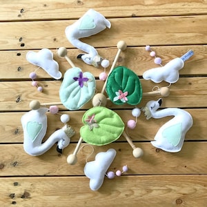 May include: A white and green felt mobile with swans, lily pads, and pink pom-poms. The mobile is suspended from a wooden dowel rod.
