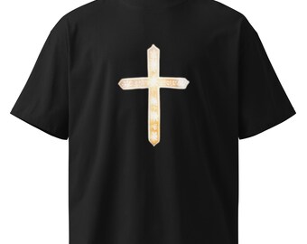 May include: Black t-shirt featuring a gold-colored cross design on the front. The cross has a detailed, textured appearance with a lighter center and a darker outline. The shirt has a crew neck and short sleeves.