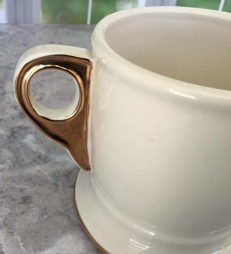 Puede incluir: Taza de cer&aacute;mica color crema con asa y borde dorados. La taza tiene una forma cl&aacute;sica con una base ancha y una parte superior redondeada. El asa es una caracter&iacute;stica distintiva que a&ntilde;ade un toque de elegancia al dise&ntilde;o.