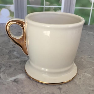 Puede incluir: Taza de cer&aacute;mica color crema con asa y borde dorados. La taza tiene una abertura ancha y una base robusta. El asa es una caracter&iacute;stica distintiva, que a&ntilde;ade un toque de elegancia al dise&ntilde;o. La taza es probablemente para bebidas.