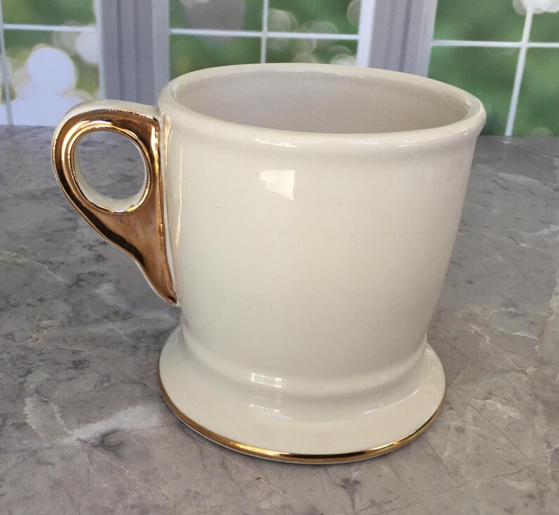 Puede incluir: Taza de cer&aacute;mica color crema con asa y borde dorados. La taza tiene una abertura ancha y una base robusta. El asa es una caracter&iacute;stica distintiva, que a&ntilde;ade un toque de elegancia al dise&ntilde;o. La taza es probablemente para bebidas.