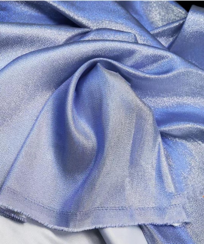 May include: A close-up of a light blue fabric with a subtle shimmer. The fabric has a smooth, silky texture and a slightly textured surface.