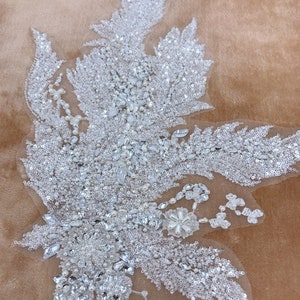 以下が含まれることがあります： 花柄の繊細な白いビーズのアップリケ。アップリケは、スパンコール、パール、クリスタルでできています。