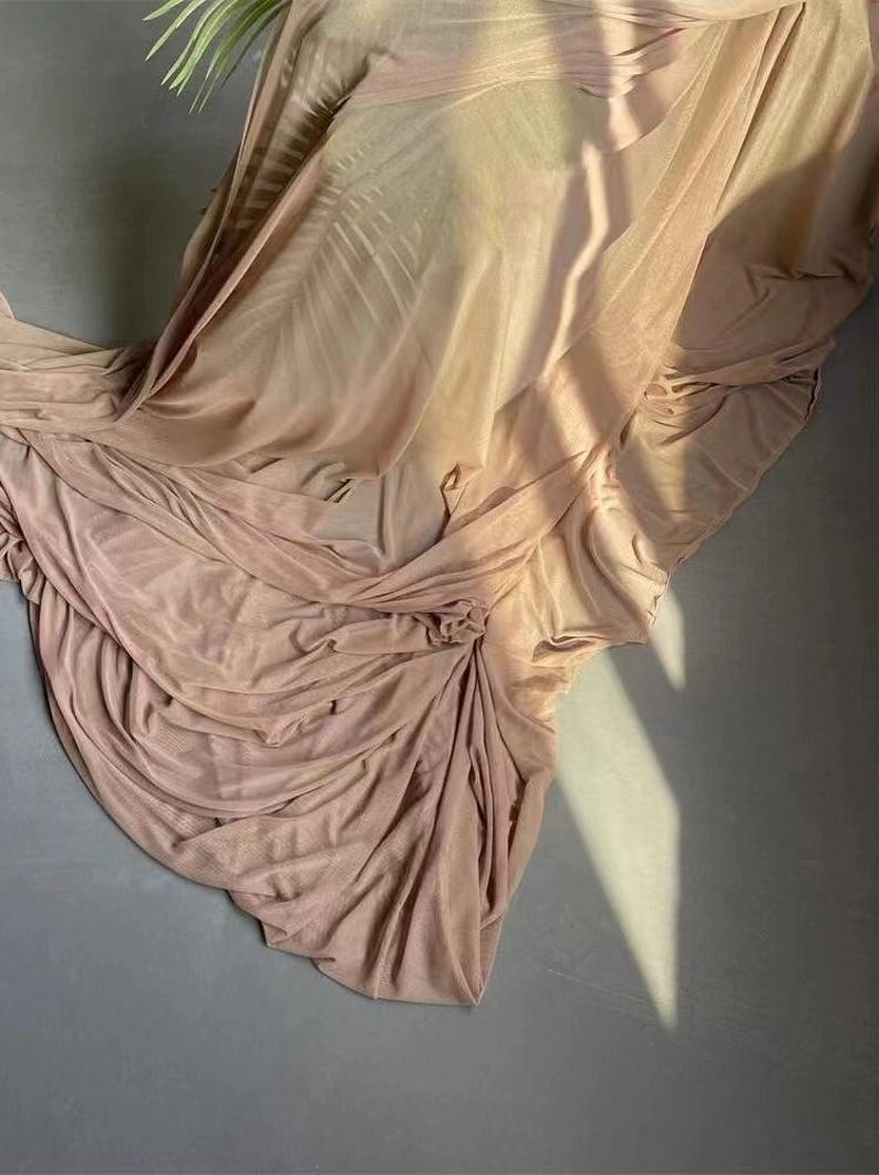May include: A soft, light pink fabric backdrop with a smooth, silky texture. The fabric is draped and folded, creating a flowing, elegant look.