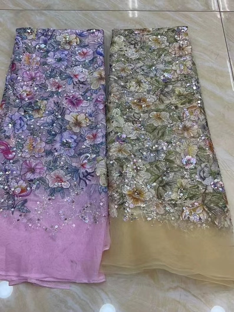 May include: Two pieces of floral embroidered fabric with sequins. The fabric on the left is pink and the fabric on the right is beige.