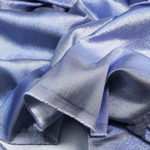 May include: Close-up of a light blue fabric with a subtle shimmer. The fabric has a smooth, silky texture and a slightly iridescent sheen.