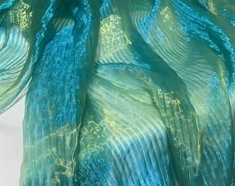Può includere: Una sciarpa leggera e trasparente caratterizzata da un vivace gradiente di turchese e verde lime. Il tessuto presenta una distinta consistenza plissettata e stropicciata con strisce verticali e una sottile finitura metallizzata.