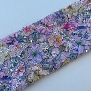 May include: A pink fabric with a floral pattern and iridescent sequins. The fabric is folded in half and the sequins are visible on both sides.