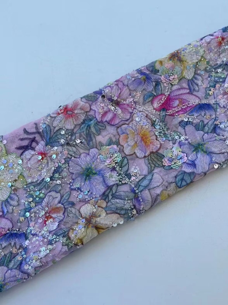 May include: A pink fabric with a floral pattern and iridescent sequins. The fabric is folded in half and the sequins are visible on both sides.