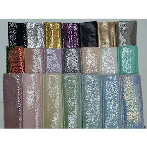 May include: A collection of colorful sequin ribbons in various shades, including black, silver, gold, purple, and teal. The ribbons are arranged side by side, showcasing their shimmering texture and reflective qualities. Ideal for crafting and embellishments.