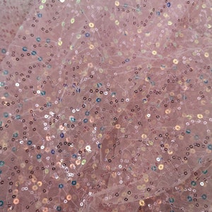 May include: Pink sheer fabric with iridescent sequins scattered throughout. The fabric is slightly wrinkled and has a soft, delicate texture.
