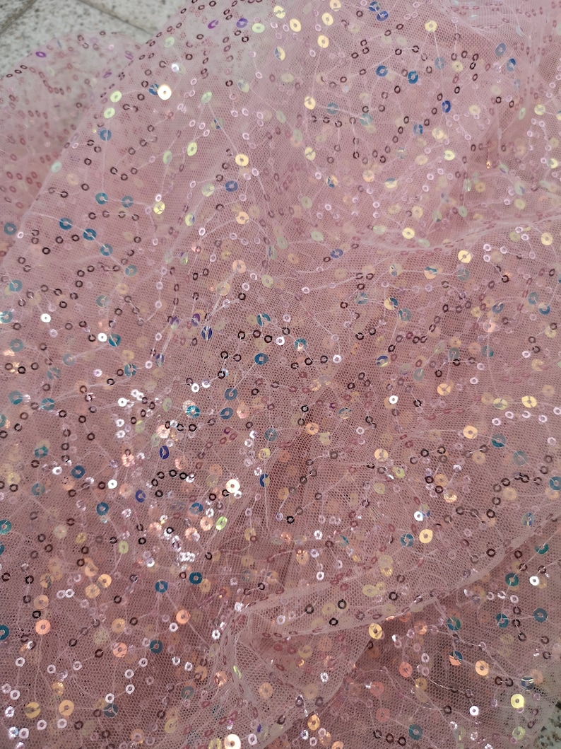 May include: Pink sheer fabric with iridescent sequins scattered throughout. The fabric is slightly wrinkled and has a soft, delicate texture.