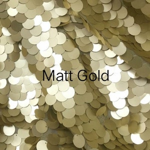 Op de afbeelding: Een close-up van een stof met een patroon van overlappende cirkels. De cirkels zijn matgoud van kleur. De tekst "Matt Gold" is zichtbaar in het midden van de afbeelding.