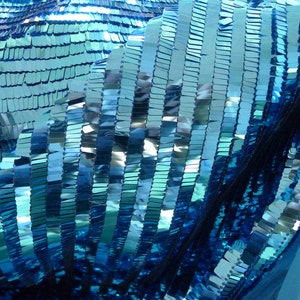 Peut inclure: Gros plan sur un tissu bleu pailleté avec une finition chatoyante et irisée. Les paillettes sont disposées en rangées verticales, créant un motif rayé.