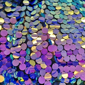 May include: A close-up of iridescent blue, purple and gold sequins on a black mesh fabric. The sequins are round and have a slightly raised centre.