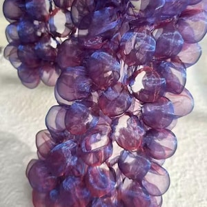 Puede incluir: Un grupo de decoraciones moradas semitransparentes en forma de orbes. Los orbes tienen una apariencia texturizada y en capas con toques de azul y rojo. El efecto general es delicado y etéreo, lo que sugiere un artículo decorativo o material de manualidades.