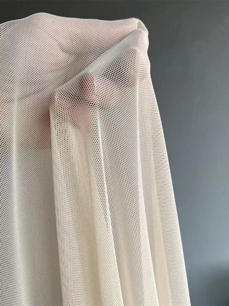 May include: A close-up of a piece of off-white mesh fabric. The fabric is very sheer and has a fine, even weave.