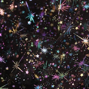 May include: Black mesh fabric with a repeating pattern of iridescent stars and fireworks. The fabric has a sparkly, glittery finish.
