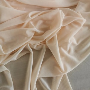 May include: A close-up of a sheer, peach-colored fabric. The fabric is soft and delicate, with a slightly textured surface.