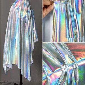 May include: A silver iridescent fabric with a holographic finish. The fabric is draped over a mannequin and shows the texture and sheen of the material.