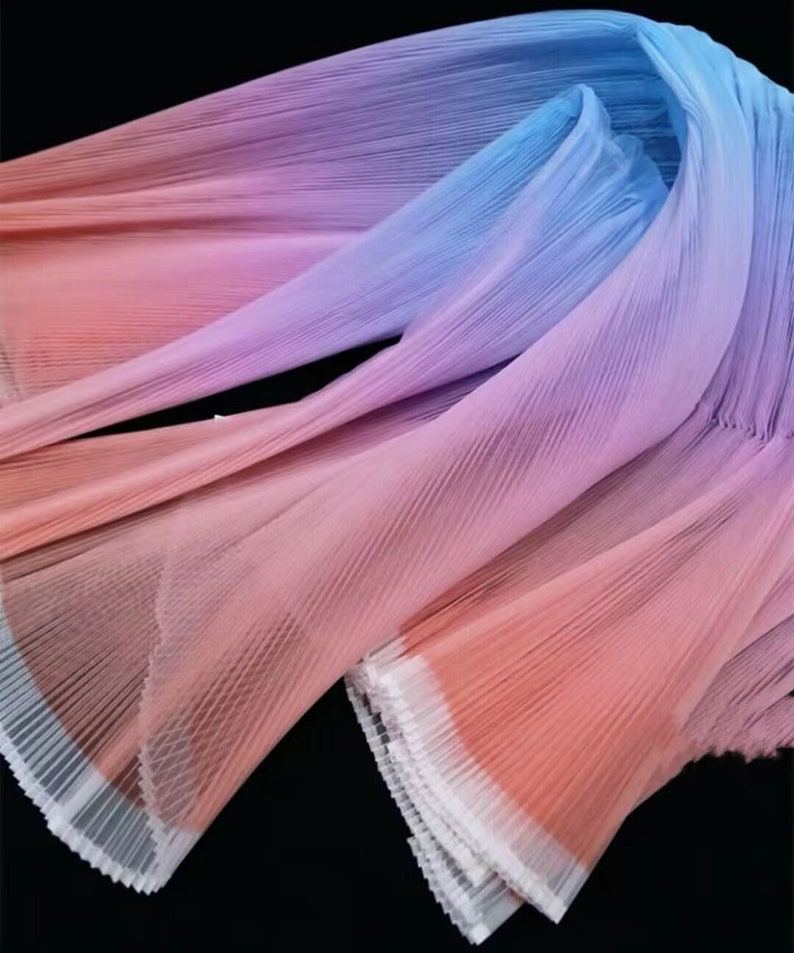 Peut inclure: Un tissu &agrave; texture pliss&eacute;e avec un d&eacute;grad&eacute; d'ombre. Le tissu est rose, violet et bleu. Le tissu est pli&eacute; et a un bord blanc.