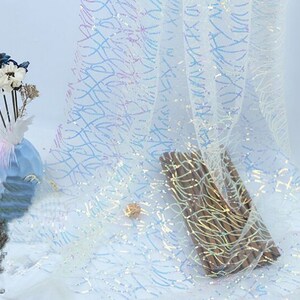 May include: White iridescent fabric with a subtle pattern of wavy lines. The fabric has a shimmery, sparkly finish.
