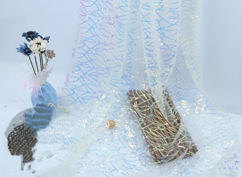 May include: White iridescent fabric with a subtle pattern of wavy lines. The fabric has a shimmery, sparkly finish.