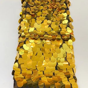 May include: Gold sequin fabric with a mesh backing. The sequins are oval shaped and arranged in a repeating pattern.