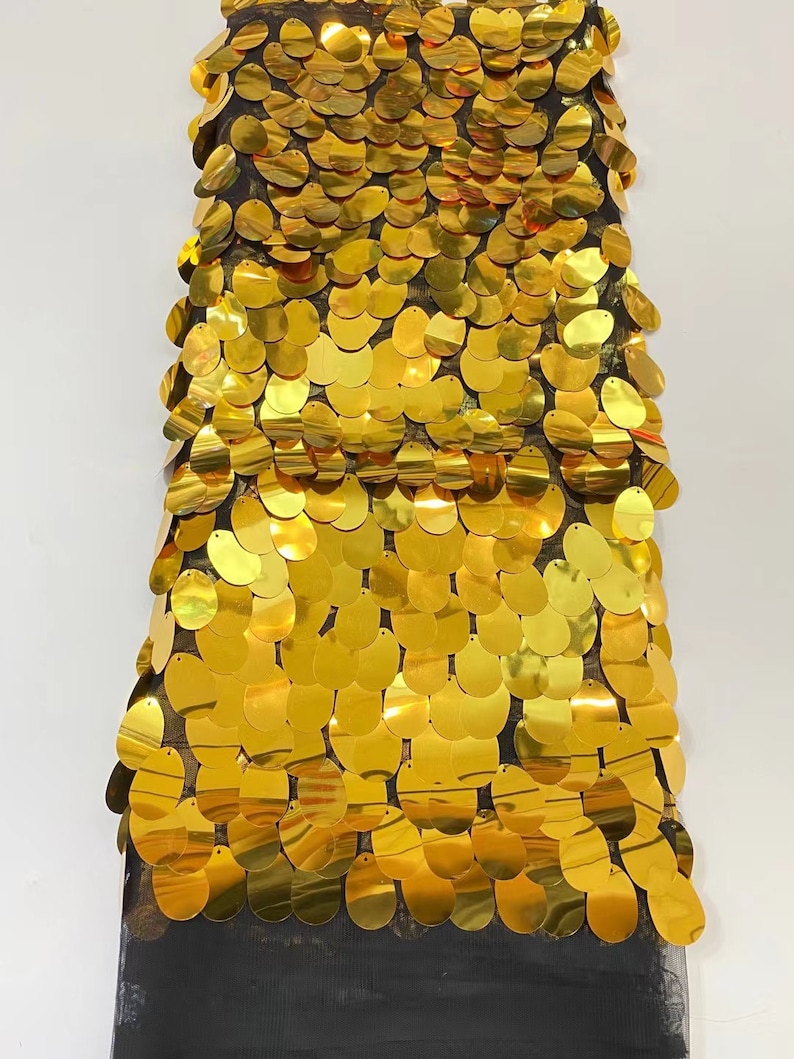 May include: Gold sequin fabric with a mesh backing. The sequins are oval shaped and arranged in a repeating pattern.