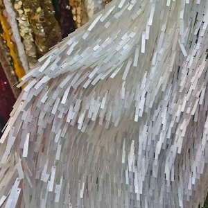 May include: A sheer fabric textile embellished with numerous white rectangular sequins arranged in a dense, overlapping fringe pattern. The sequins are attached at one end, creating a cascading, layered effect across the surface of the material.