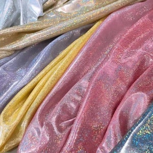 May include: A stack of iridescent fabric in various colours, including pink, yellow, silver, and white. The fabric has a shimmery, glittery texture.
