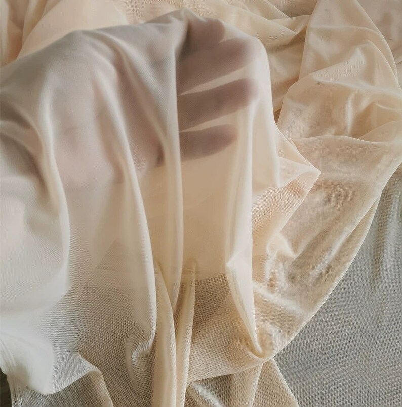 May include: A sheer, lightweight fabric in a pale beige color. The fabric is very delicate and has a soft, flowing texture.