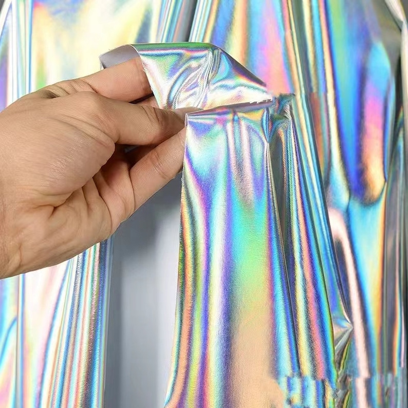 May include: A close-up of iridescent silver fabric with a holographic finish. The fabric is smooth and has a subtle sheen.