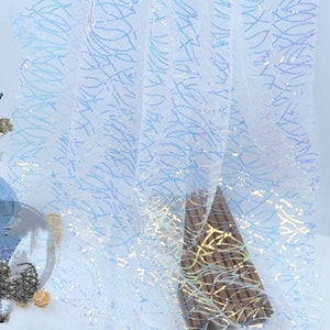 May include: White iridescent fabric with a blue and gold pattern. The fabric is sheer and has a delicate texture.