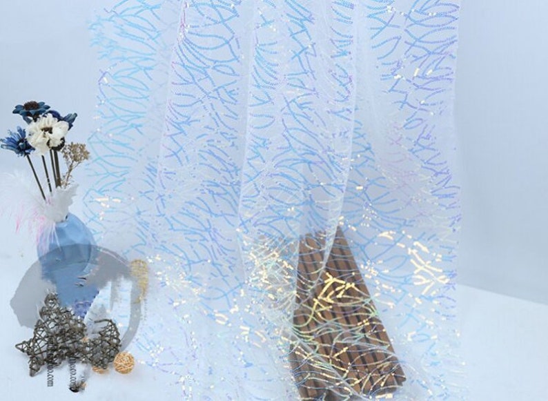 May include: White iridescent fabric with a blue and gold pattern. The fabric is sheer and has a delicate texture.