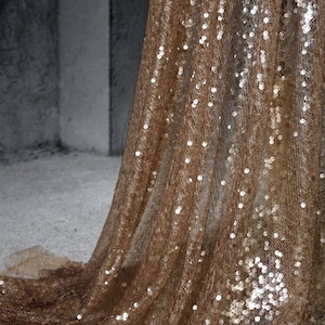 Op de afbeelding: Een close-up van een bruine stof met zilveren pailletten. De stof is over een oppervlak gelegd en heeft een zachte, glinsterende textuur.