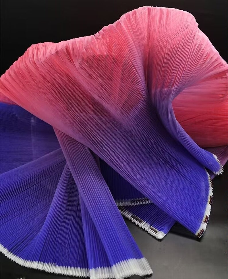 Peut inclure: Un tissu pliss&eacute; avec un d&eacute;grad&eacute; de couleurs, passant du rose au violet. Le tissu est pli&eacute; et dispos&eacute; en forme de vague.