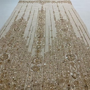 May include: Ivory fabric with detailed gold bead and sequin embellishments. The design includes elaborate patterns with vertical and circular motifs. Ideal for bridal wear, evening gowns, or special occasion garments. The fabric is measured in centimetres.